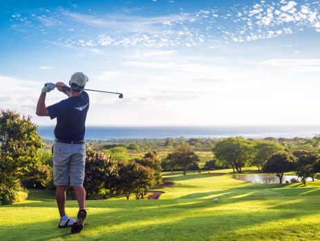 Man hitting golf ball down hill towards ocean and horizon